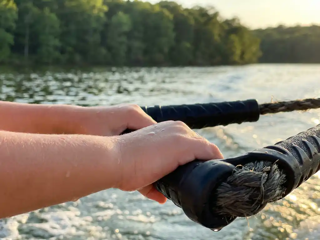 Natte kinderhanden grijpen een kneeboard-touwhandvat, waterdruppels glinsteren in warm zomerlicht boven een Nederlands meer.