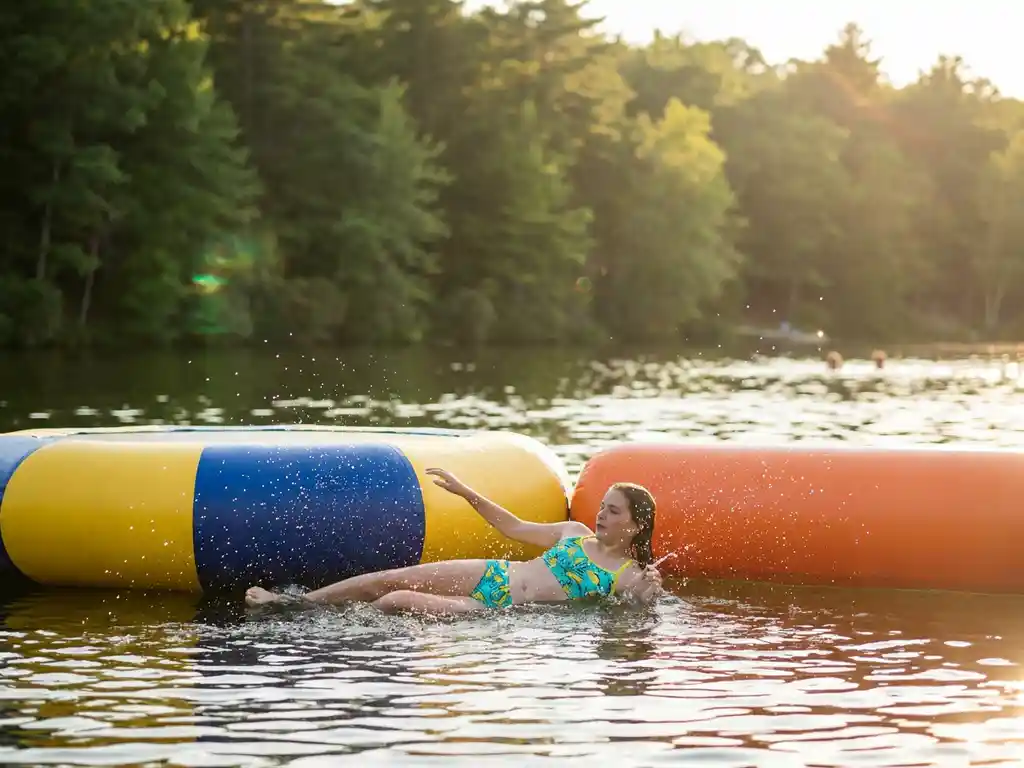 Kind op kleurrijk opblaasbaar parcours in zonnig meer, waterdruppels in gouden namiddaglicht, Nederlands bos weerspiegelt in kalm water.